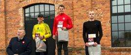 Zwycięstwo asp. Piotra Domańskiego w 11. Bieg Niepodległości - pod budynkiem stoją zawodnicy w dresach w rękach mają dyplomy i nagrody, 