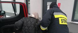  Na zdjęciu widzimy jak strażak pomaga przejść starszej osobie po śliskiej nawierzchni do ośrodka szczepień.