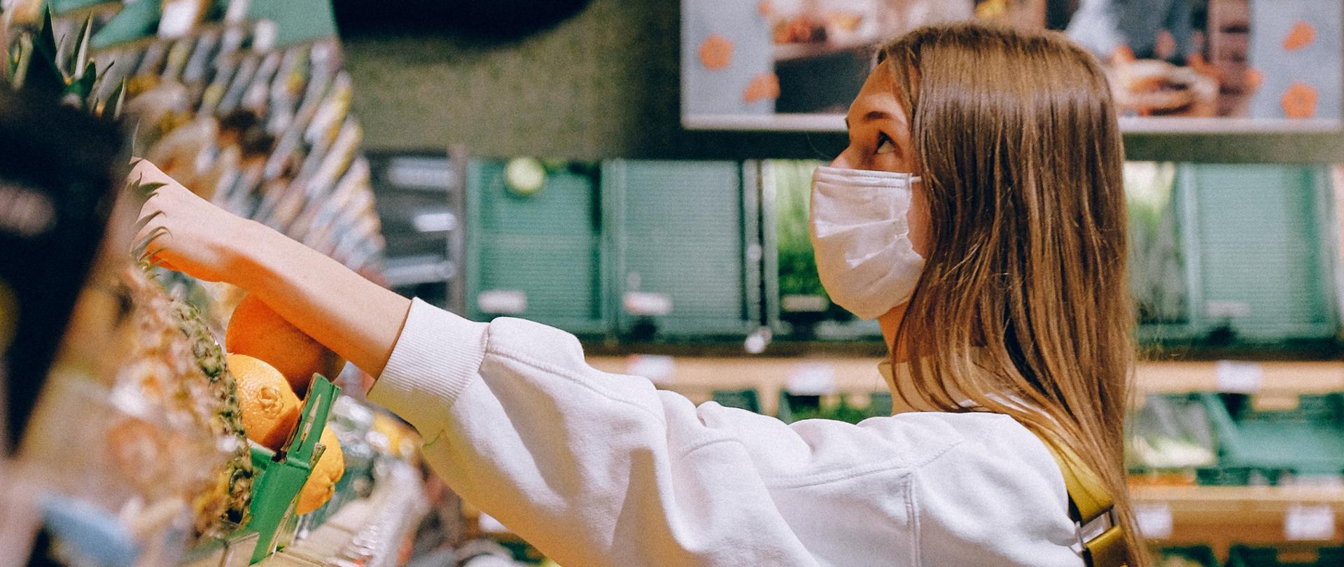 Kobieta w maseczce ochronnej dokonuje zakupów w sklepie