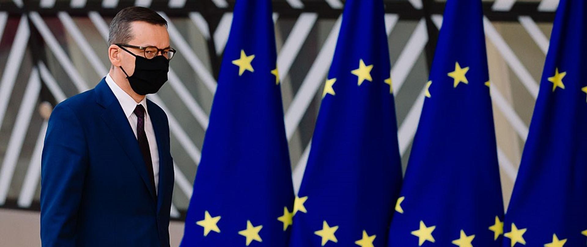 Premier Mateusz Morawiecki idzie na tle flag UE.