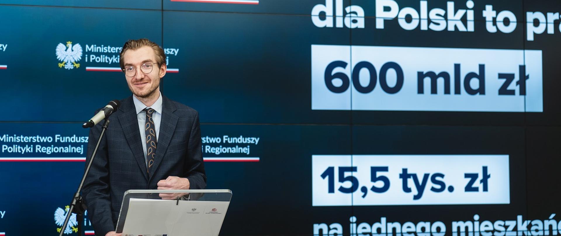 Wiceminister funduszy i polityki regionalnej Jan Szyszko na konferencji prasowej w MFiPR, za plecami wiceministra grafika informująca o 600 mld zł z Funduszy Europejskich dla Polski 
