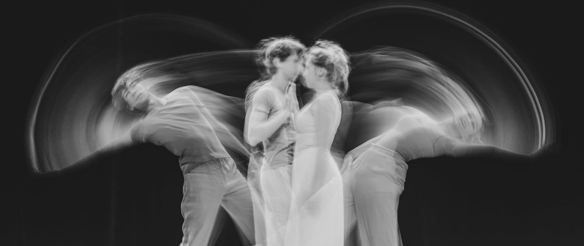 Zdjęcie jest w kolorystyce czarno-białej. Po środku kardu stoi para w tanecznej pozie. Zdjęcie ma efekt rozmycia. 