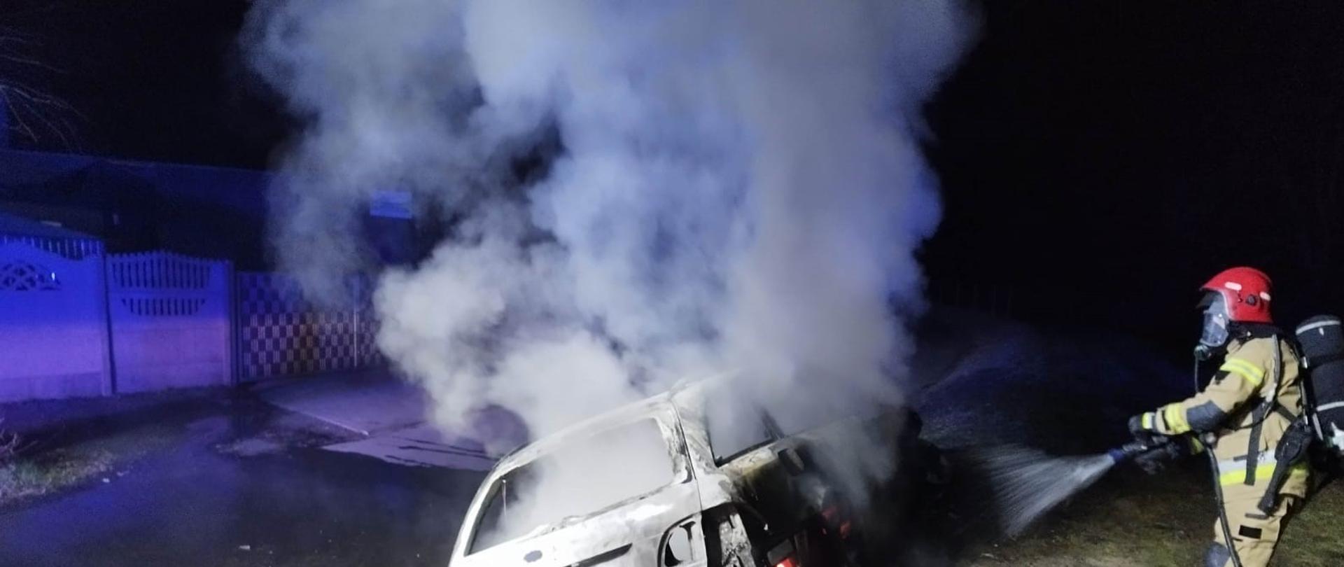 Zdjęcie przedstawia strażaka podającego prąd gaśniczy na pojazd, który objęty jest pożarem.