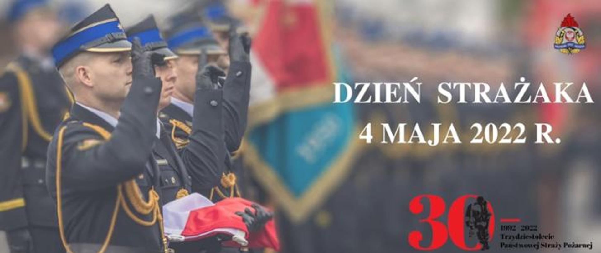 Strażacy w mundurach wyjściowych stoją prawym bokiem w rzędzie, salutują. jeden z nich trzyma złożoną flagę. Widnieje napis: Dzień Strażaka 4 maja 2022 r. logo PSP oraz logo 30-lecia Państwowej Straży Pożarnej.