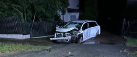 Na zdjęciu widoczny jest samochód osobowy Toyota Avensis z uszkodzonym przodem w wyniku wypadku drogowego. Samochód znajduje się na wjeździe do posesji. 