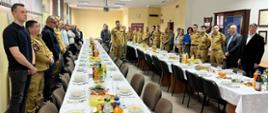 Funkcjonariusze, pracownicy cywili oraz emeryci stoją przy zastawionych potrawami i napojami stołach słuchając składanych życzeń z okazji Świąt Wielkanocnych.