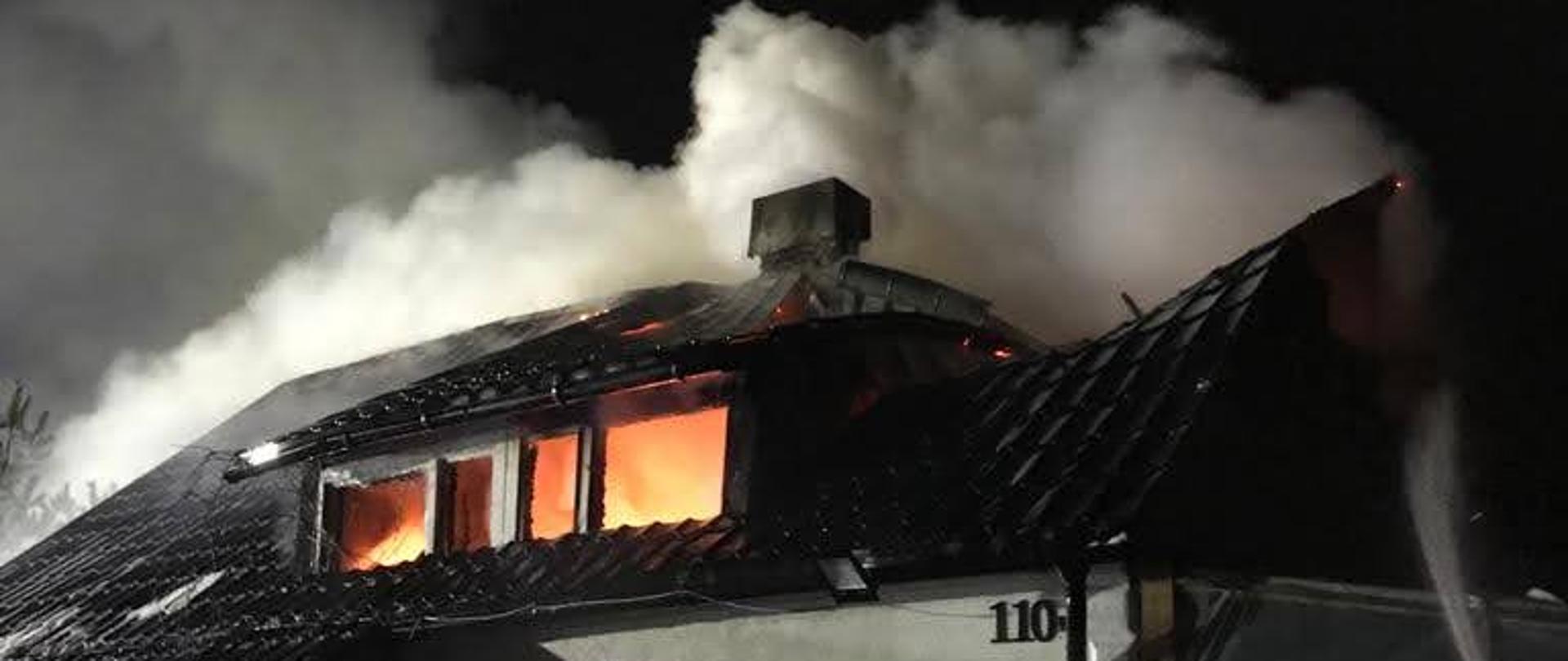 Kłęby dymu nad budynkiem i widoczne płomienie w oknach na poddaszu