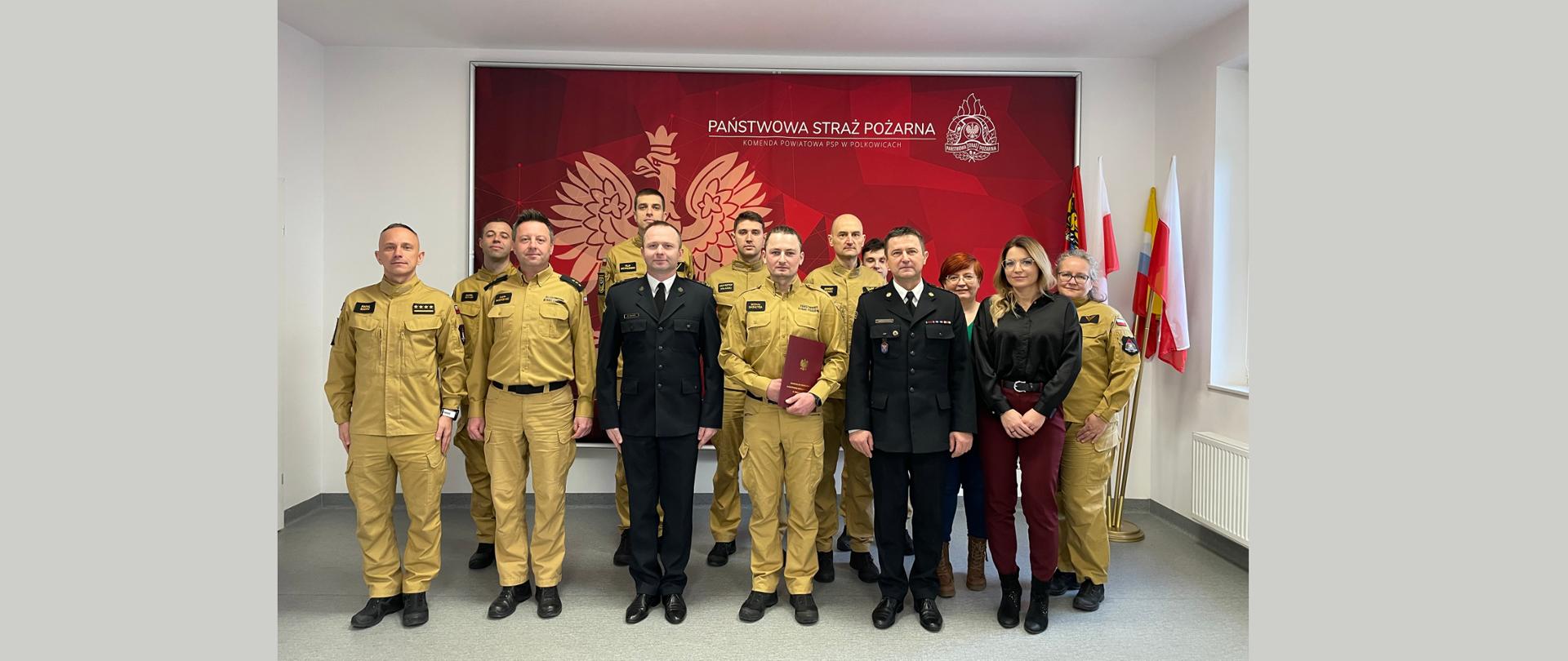 Zdjęcie grupowe strażaków KP PSP w Polkowicach na tle godła