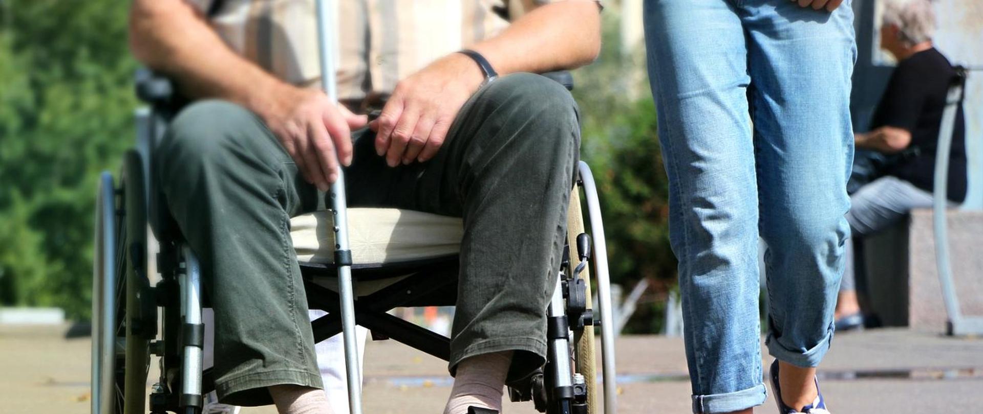 człowiek na wózku obok osoba idzie na nogach