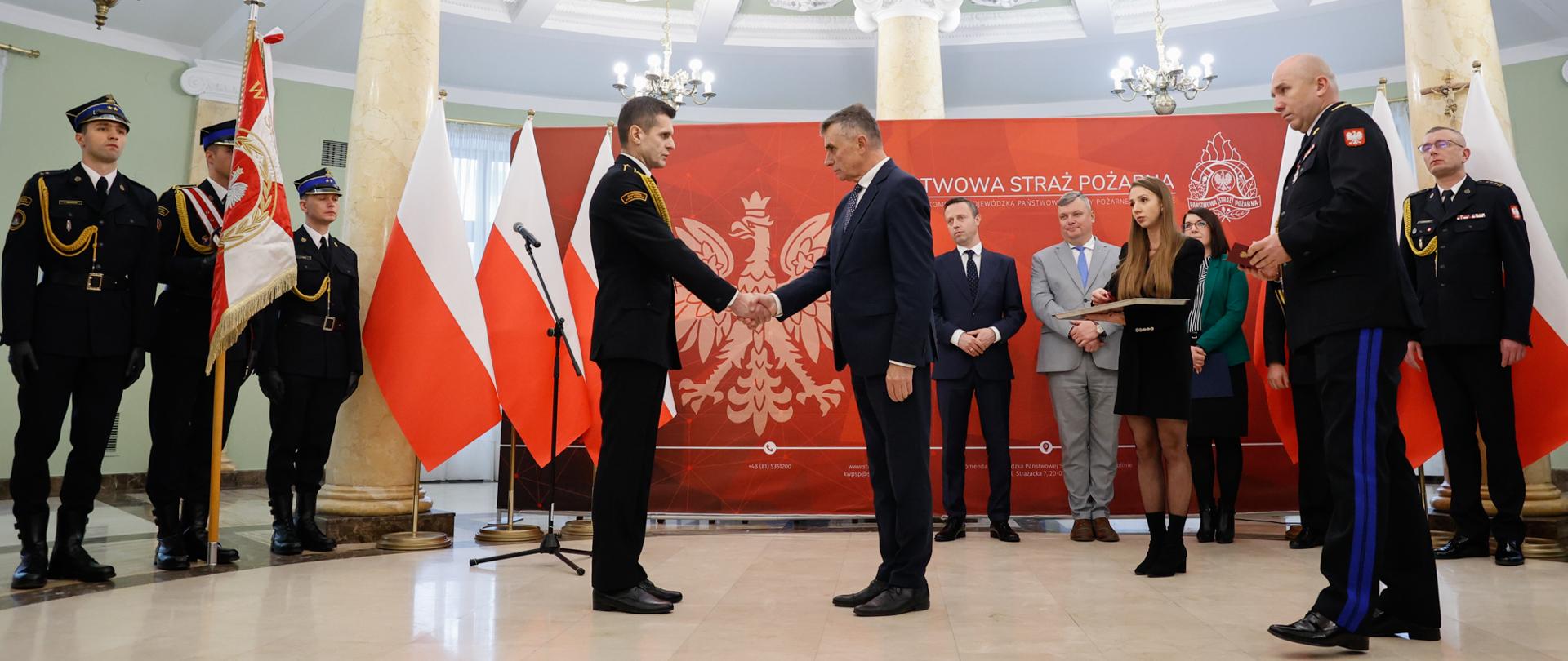 Uroczysta zbiórka z okazji Narodowego Święta Niepodległości. Wojewoda lubelski gratuluje strażakowi.