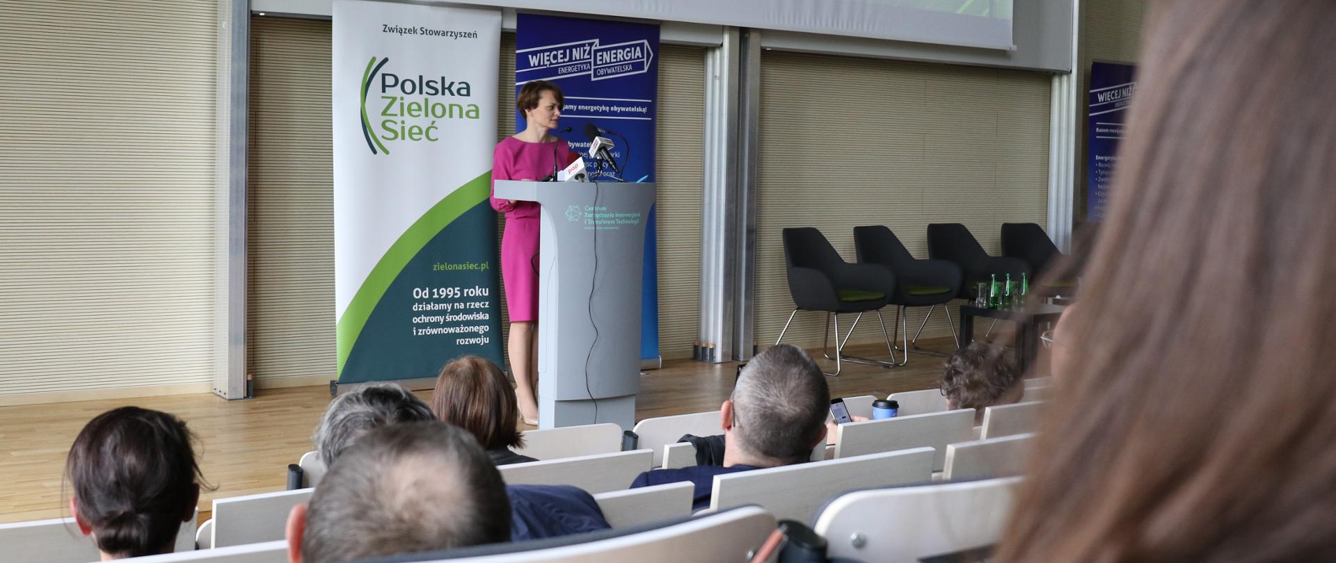 Jadwiga Emilewicz przy mównicy opowiada o programie Energia Plus na III Kongresie Energetyki Obywatelskiej. Stoi na scenie. Za nią prezentacja z napisem "energia".