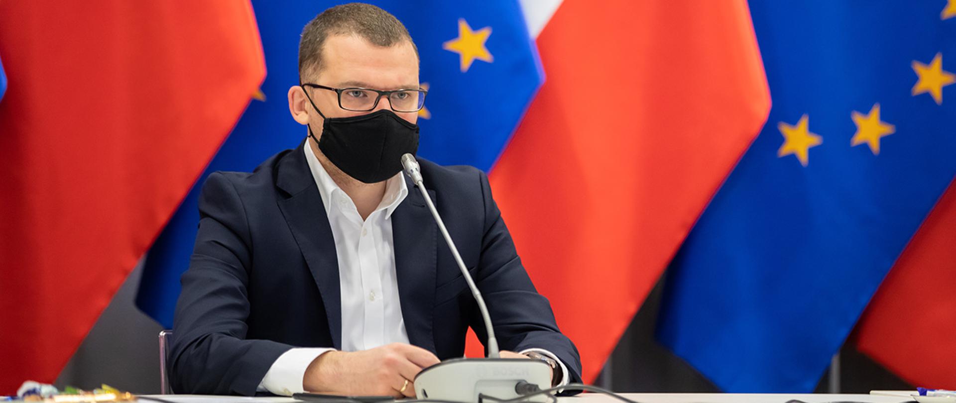 Na zdjęciu widać wiceministra Pawła Szefernakera siedzącego za stołem na tle flag Polski i UE.