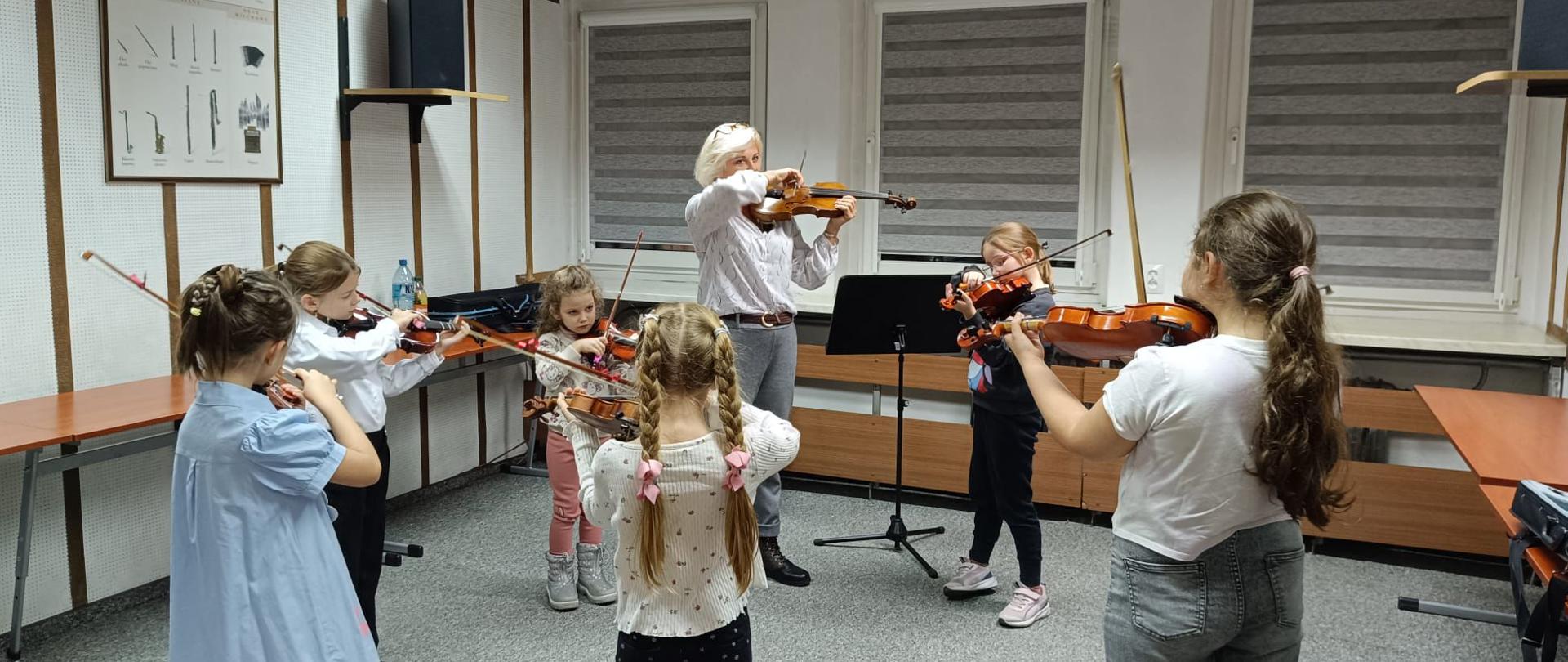 Sześć dziewczynek i kobieta stoi w kole i grają na skrzypcach.