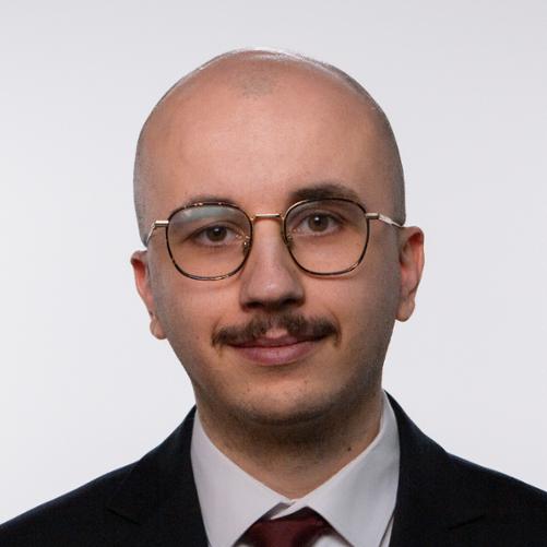 Portret Marcina Malecko - uśmiechający się mężczyzna w garniturze na jednolitym tle