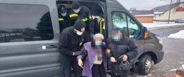 Druhowie OSP Mikołajki Pomorskie pomagają podczas transportu osoby starszej przemieścić się z pojazdu do punktu szczepień.