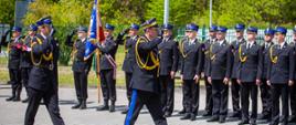 Na zdjęciu widoczni Małopolski Komendant Wojewódzki PSP oraz dowódca uroczystości udający się do przeglądu poddziałów. Strażacy w umundurowaniu galowym koloru granatowego w czapkach rogatywkach ze sznurem. W tle widoczne samochody pożarnicze.