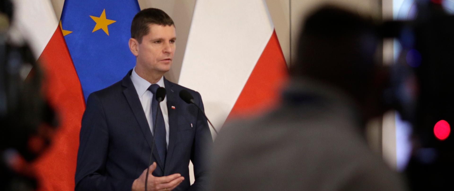 Na mównicy przemawia minister edukacji. W tle flaga Polski i Unii Europejskiej 