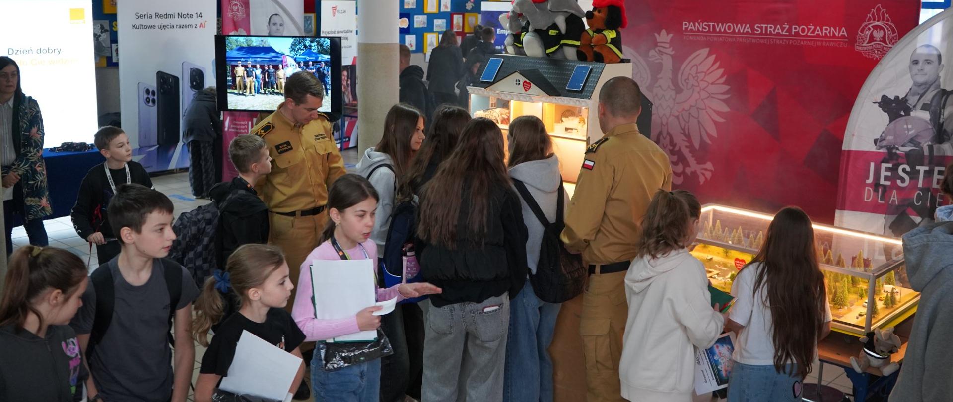  Stoisko KP PSP w Rawiczu Strażacy prowadzą zajęcia edukacyjne przy mobilnym symualatorze zagrożeń. Wtle Sierakowieścianka promocyjna oraz monitor, na którym wyświetlane są zdjęcia z akcji strażackich