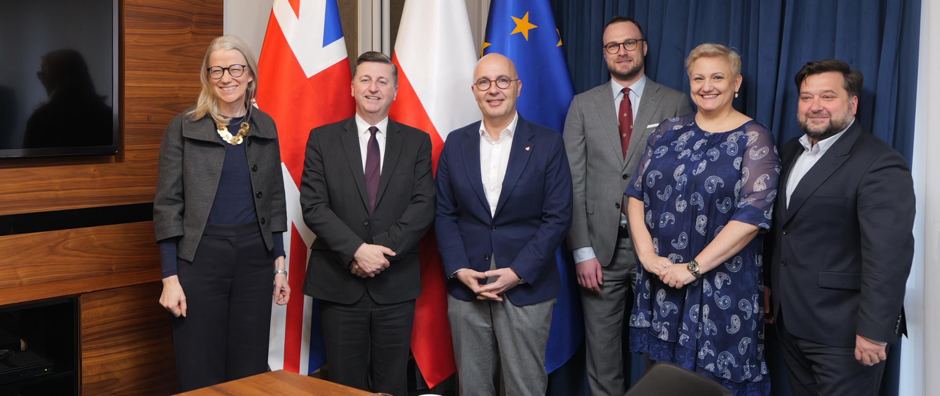 Wiceminister Robert Kropiwnicki, Minister Stanu ds. Polityki Handlowej i Bezpieczeństwa Ekonomicznego w Departamencie Biznesu i Handlu Wielkiej Brytanii, Douglas Alexander oraz przedstawiciele MAP stoją na tle flag. 