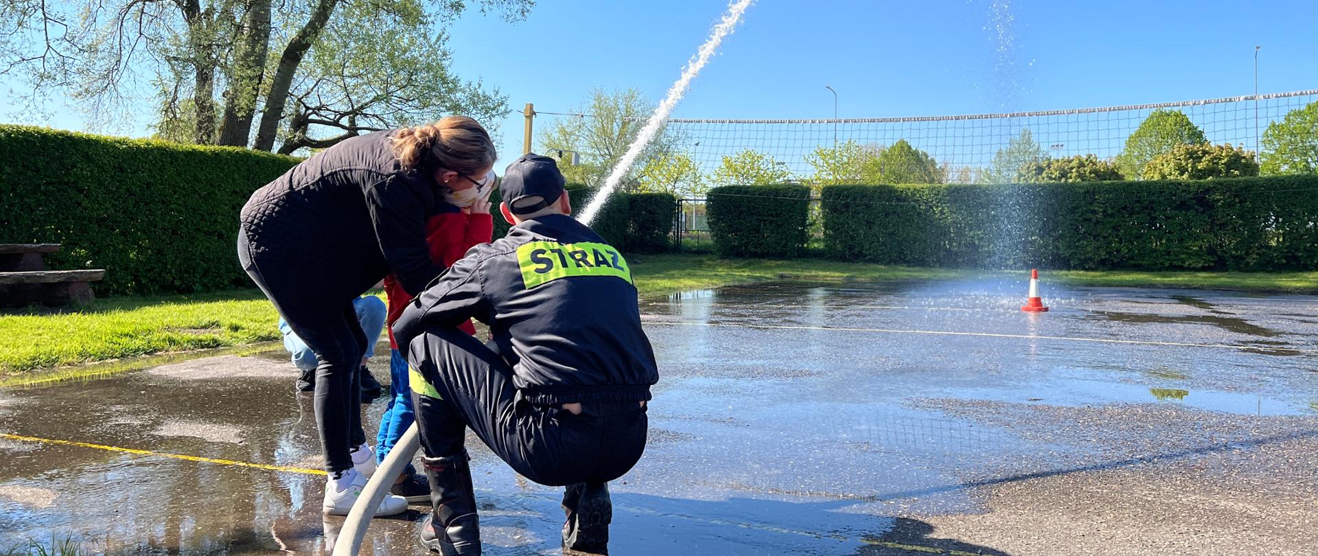 Funkcjonariusz komendy PSP w Kwidzynie prezentuje dziecku sposób podawania wody.