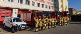 Na zdjęciu widać strażaków w umundurowaniu specjalnym podczas zmiany służby. Dowódcy zmian oddaj honor przez salutowanie. Zbiórka odbywa się przed wystawionymi samochodami ratowniczo-gaśniczymi JRG w Tucholi. Na drugim planie budynek głównym Komendy Powiatowej PSP w Tucholi.