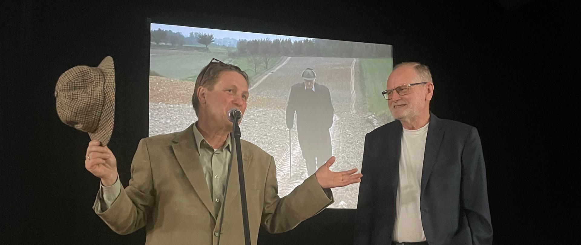 Krzysztof Hejke i Zbigniew Strzyżyński stojący na tle kadru z filmu o Jerzym Mierzejewskim