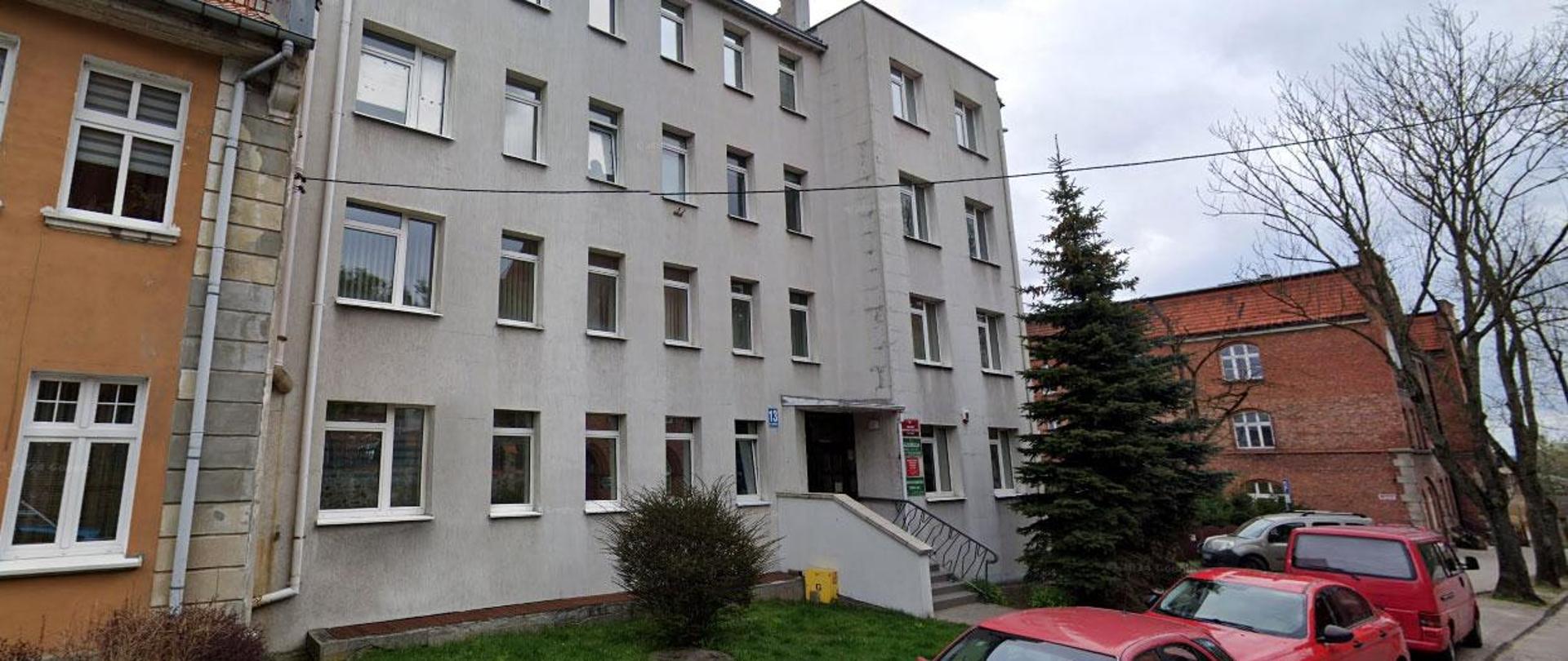 Trzypiętrowy budynek biurowy z jasnoszarą elewacją, usytuowany przy ulicy.