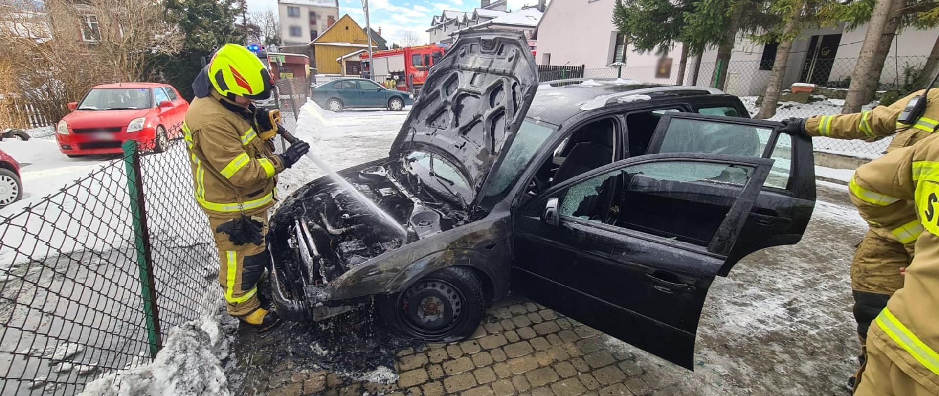 Strażak podaję prąd wody na komorę silnika samochodu