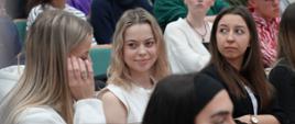 Widok z boku na wypełnioną siedzącymi ludźmi salę, na pierwszym planie kilka młodych kobiet.