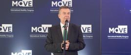 Minister Wieczorek stoi i mówi do mikrofonu na stojaku, za nim granatowa ścianka z napisem MOVE.