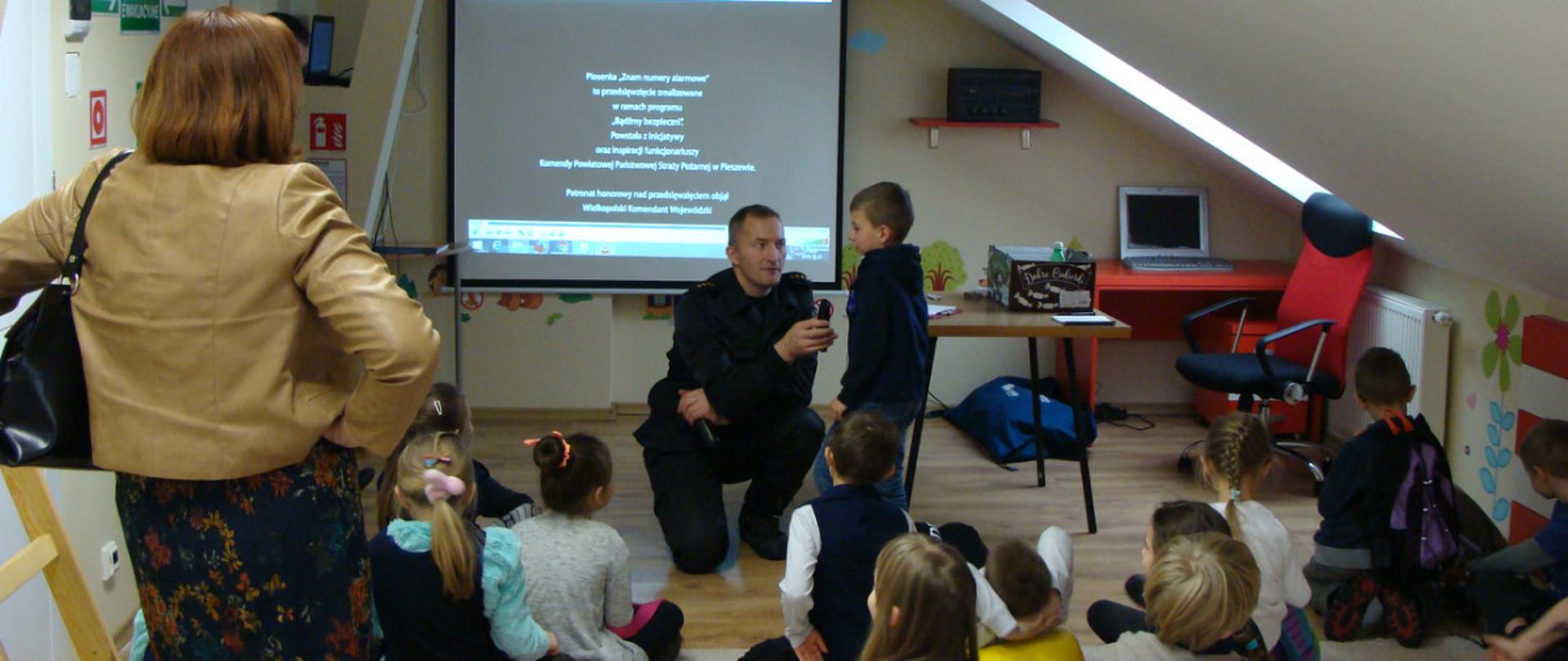 .Dzieci w sali edukacyjnej "Ognik" z funkcjonariuszem prowadzącym zajęcia. 