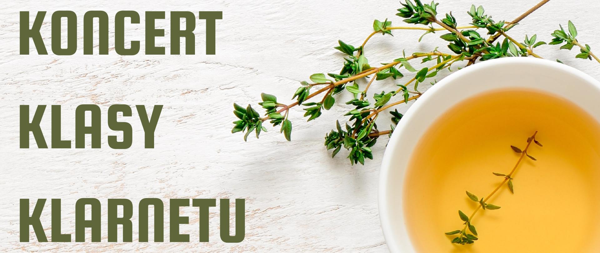 Zdjęcie dzbanka i filiżanki w kolorze białym z napojem jasnej herbaty w filiżance. Liternictwo zielone z informacją o koncercie. Wokół porcelany leżące gałązki herbaty.
