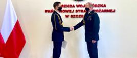 Na zdjęciu Panowie Komendanci w umundurowaniu wyjściowym podczas uścisku dłoni. W tle napis na ścianie: Komenda Wojewódzka Państwowej Straży Pożarnej w Szczecinie oraz flaga Polski.