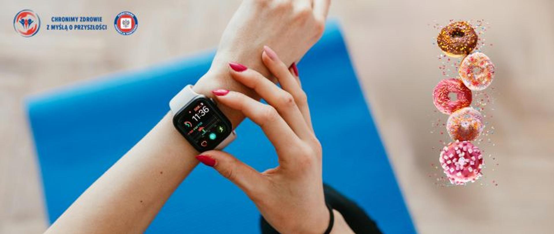 Beżowe tło. na pierwszym planie ręka kobiety, która ustawia zegarek fitness umieszczony na nadgarstku drugiej ręki. W tle mata do ćwiczeń. Po prawej stronie pączki w różnych polewach i posypkach w kolorach: brązowym, różowym. W lewym górnym rogu logo Państwowej Inspekcji Sanitarnej wraz z hasłem Chronimy zdrowie z myślą o przyszłości. 