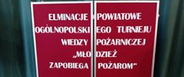 Zdjęcie przedstawia tablicę z napisem: "Eliminacje Powiatowe Ogólnopolskiego Turnieju Wiedzy Pożarniczej - Młodzież zapobiega pożarom"