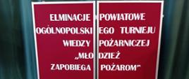 Zdjęcie przedstawia tablicę z napisem: "Eliminacje Powiatowe Ogólnopolskiego Turnieju Wiedzy Pożarniczej - Młodzież zapobiega pożarom"