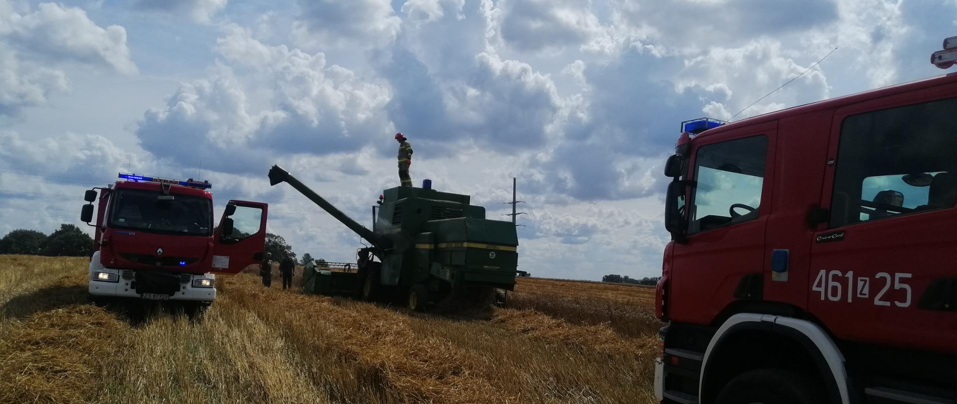Zdjęcie przedstawia kombajn oraz dwa wozy strażackie na polu