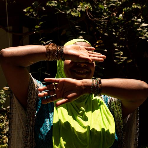 Kobieta stojąca w ostrym słońcu, zasłaniająca ręką górną część twarzy.