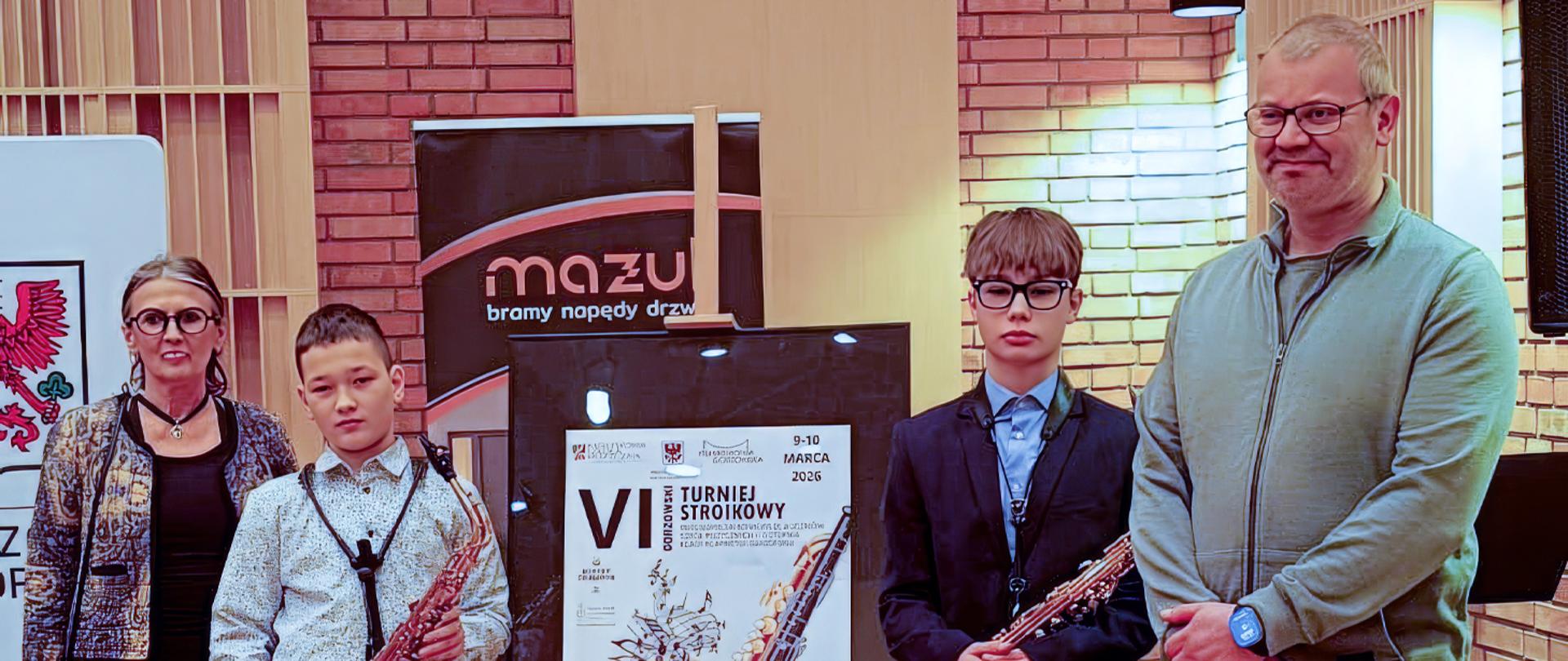 Na zdjęciu dwoje nauczycieli i dwóch uczniów, uczniowie trzymają w rękach saksofony.