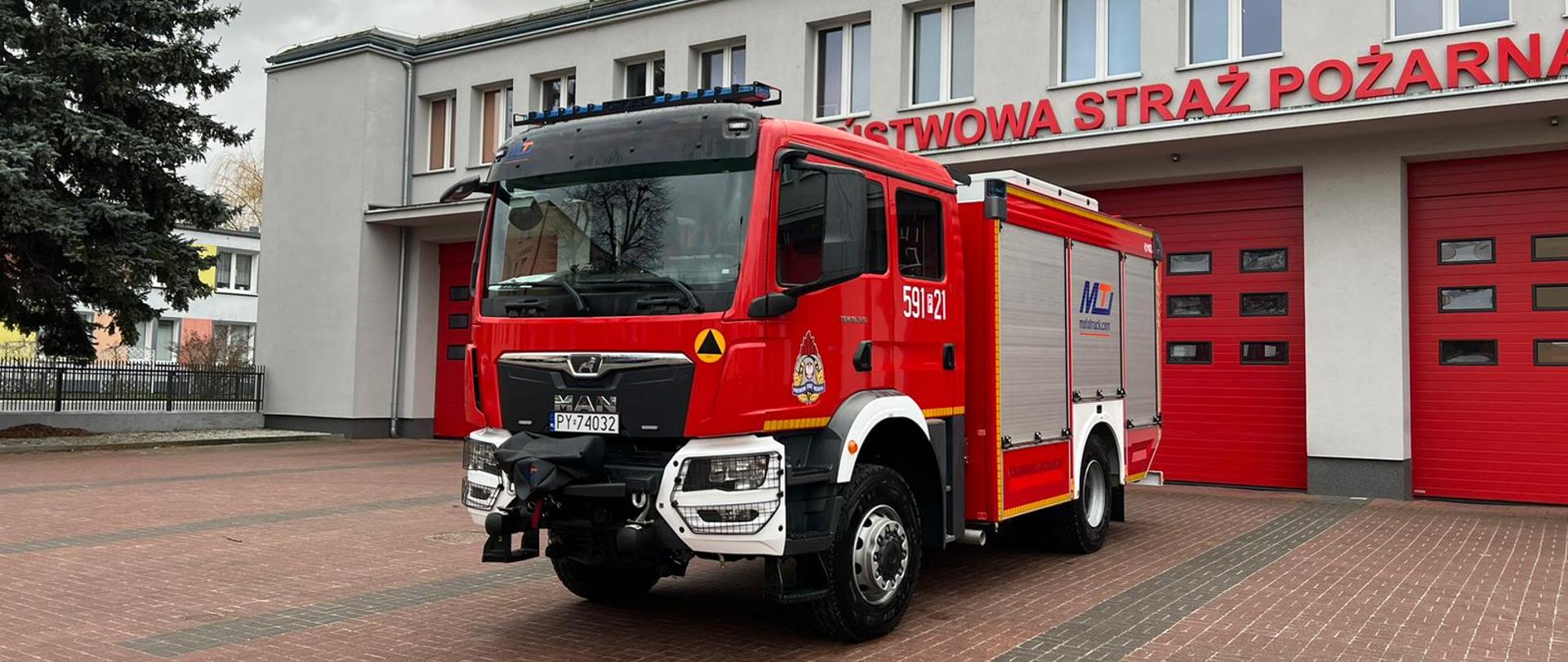 Czerwony samochód na tle budynku straży, widok od przodu