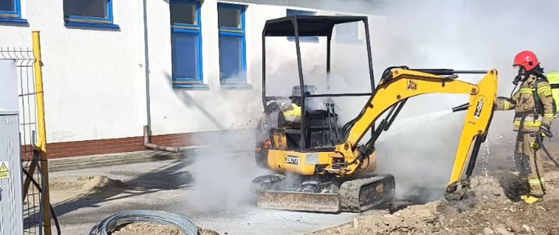 Strażak gasi pożar minikoparki obok słupa energetycznego