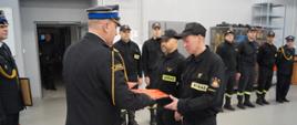 Zdjęcie przedstawia dwóch strażaków odbierających od Komendanta awanse. Po prawej stronie w rzędzie stoją strażacy.