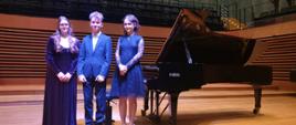 Dwie dziewczyny i chłopak stoją przy fortepianie Fazioli na scenie sali koncertowej PSM w Jastrzębiu-Zdroju