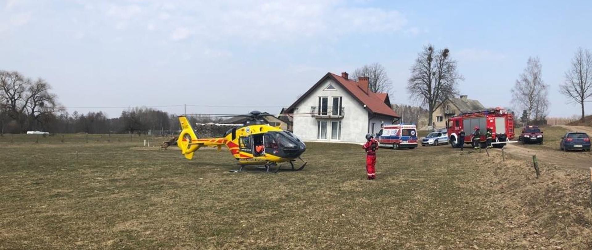 Zdjęcie przedstawia śmigłowiec Lotniczego Pogotowia Ratunkowego. W tle widać samochody Straży Pożarnej, Policji oraz Pogotowia Ratunkowego.
