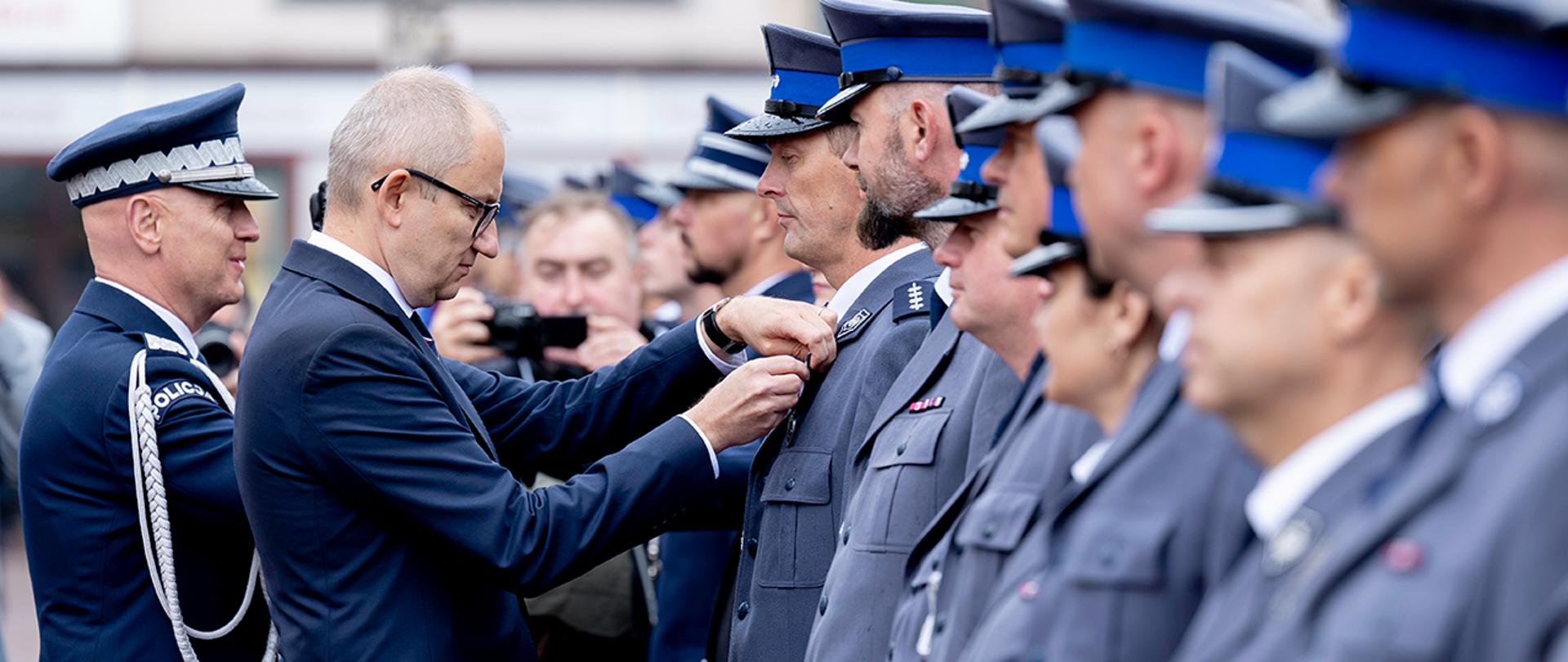 Wiceminister Błażej Poboży wpinający odznaczenie policjantowi podczas Święta Policji w Nowym Mieście Lubawskim.