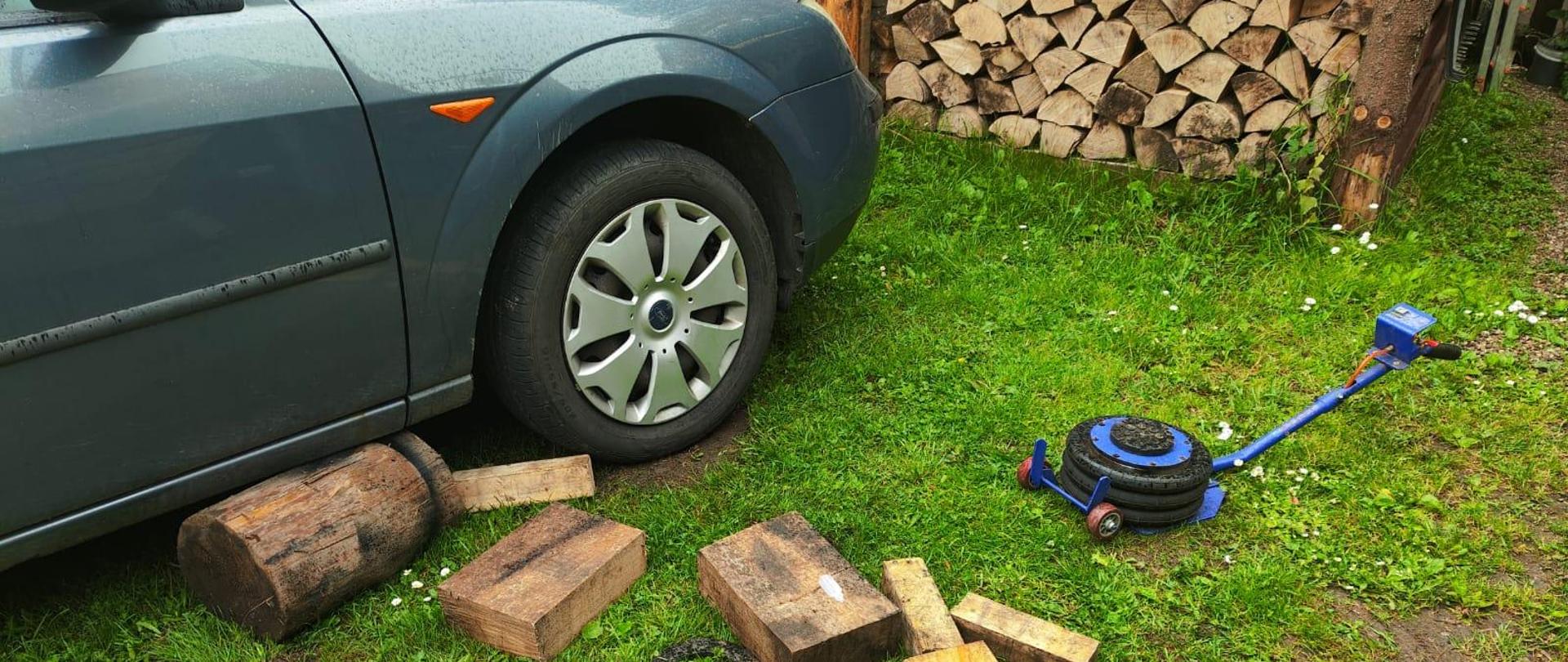 Fragment samochodu a obok drewniane klocki oraz podnośnik