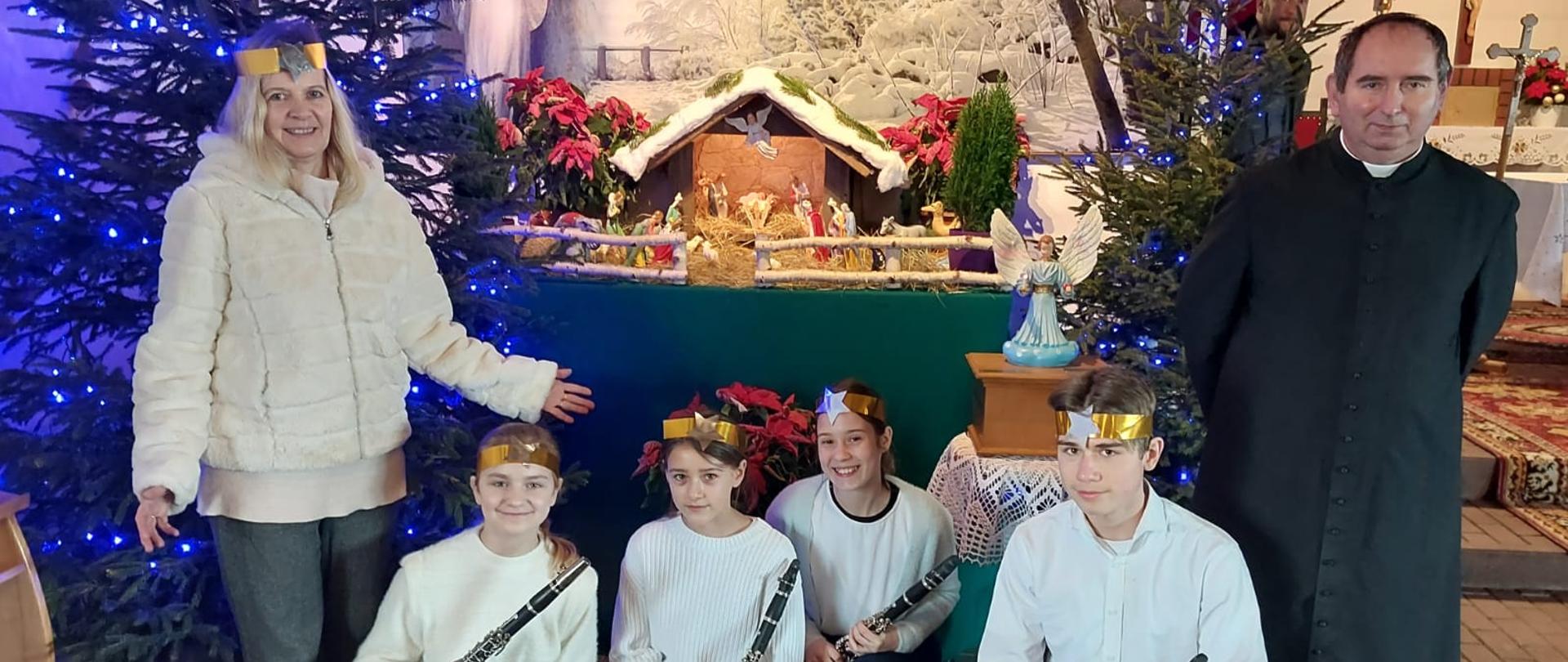 W kościele na tle szopki pozują do zdjęcia kolejno od lewej: Anna Łysko, kwartet klarnetowy oraz ksiądz. 