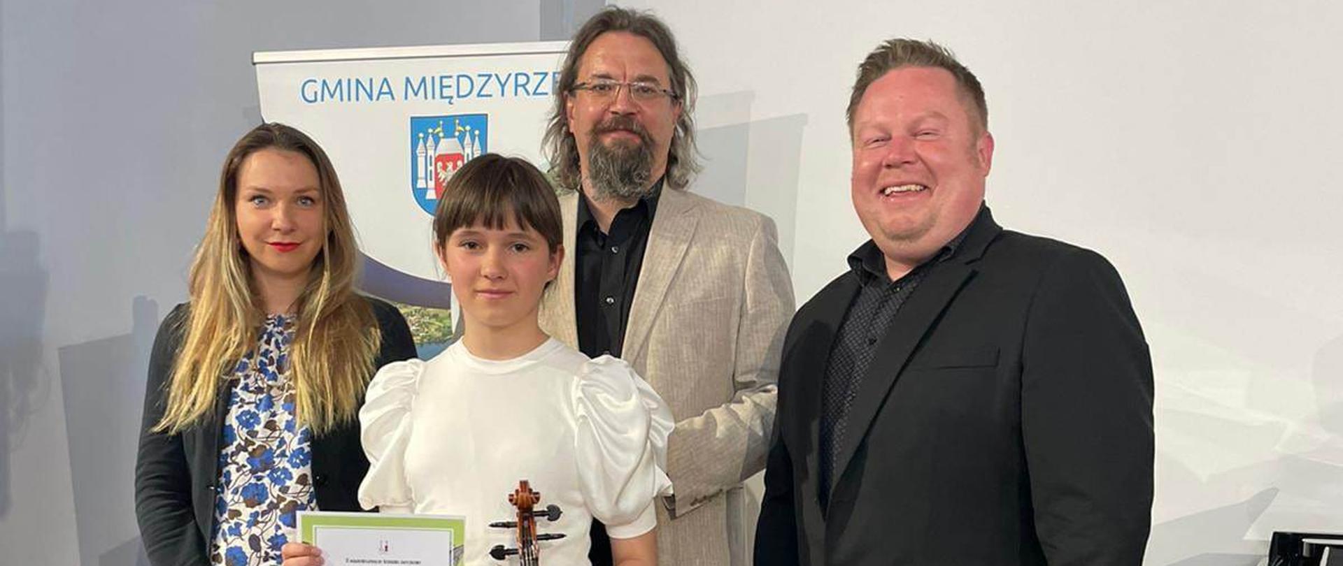 Uczennica Aleksandra Rytlewska stoi z dyplomem i skrzypcami wraz z jurorami konkursu smyczkowego