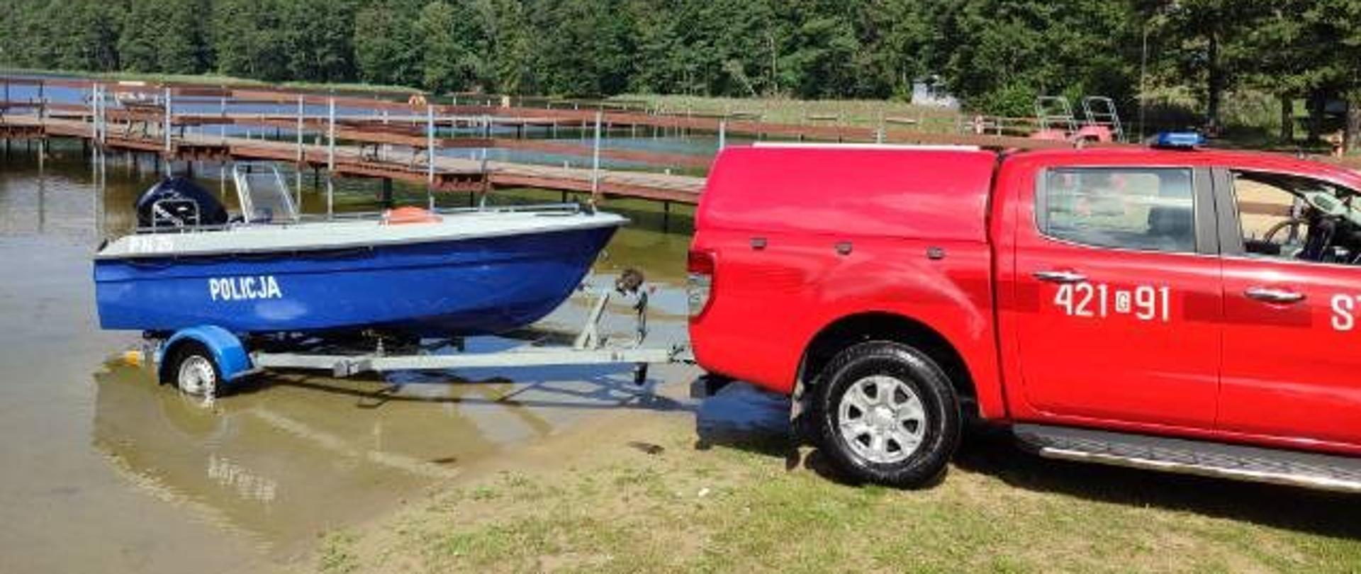 Samochód operacyjny KP PSP z policyjną łódką na przyczepce na tle jeziora.