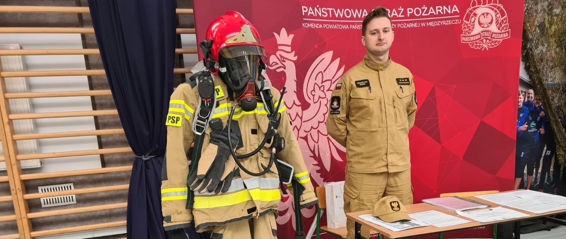 Zdjęcie przedstawia funkcjonariusza PSP na stanowisku przygotowanym aby udzielać informacji o naborze do służby. Rozpoznawalna ścianka z logo PSP, ubranie specjalne strażaka ratownika, oficer służący pomocą i odpowiadający na pytania zainteresowanych pracą w PSP osób.